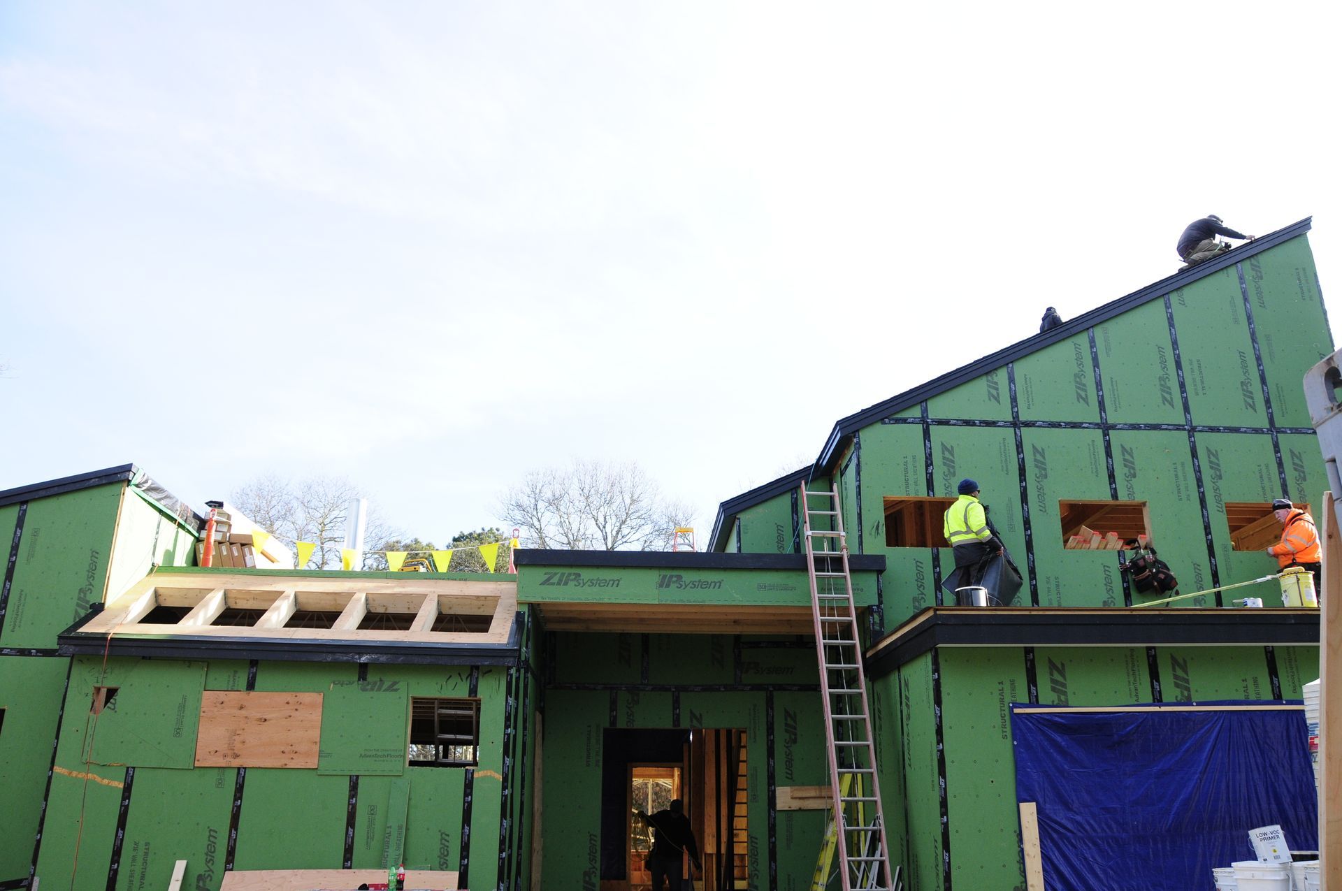 House under construction with green ZIP System sheathing and crew working on the roof