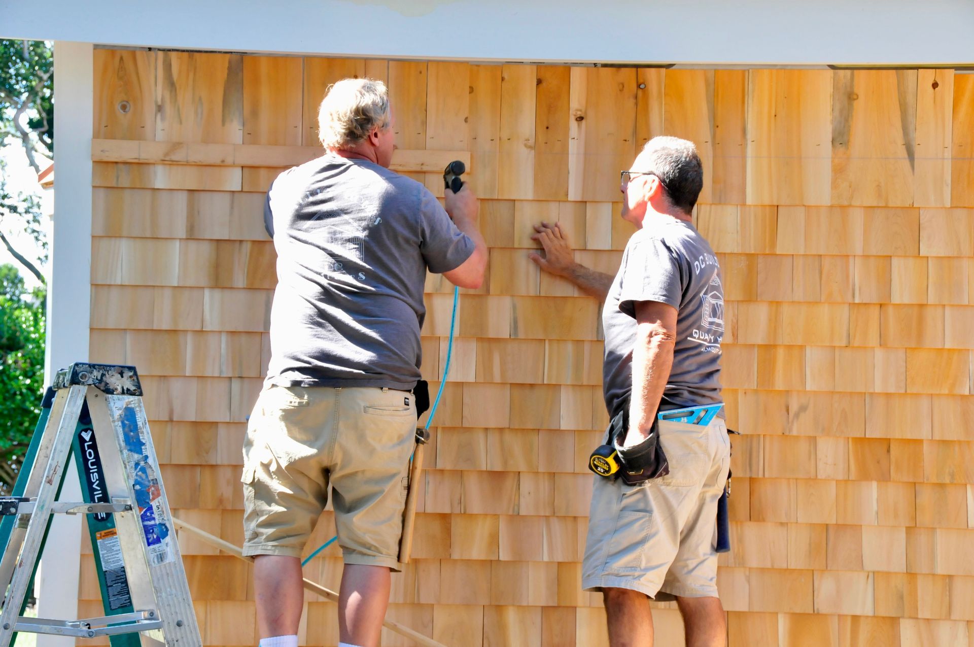 Two DC Builders carpenters installing cedar shingle siding on a Cape Cod home